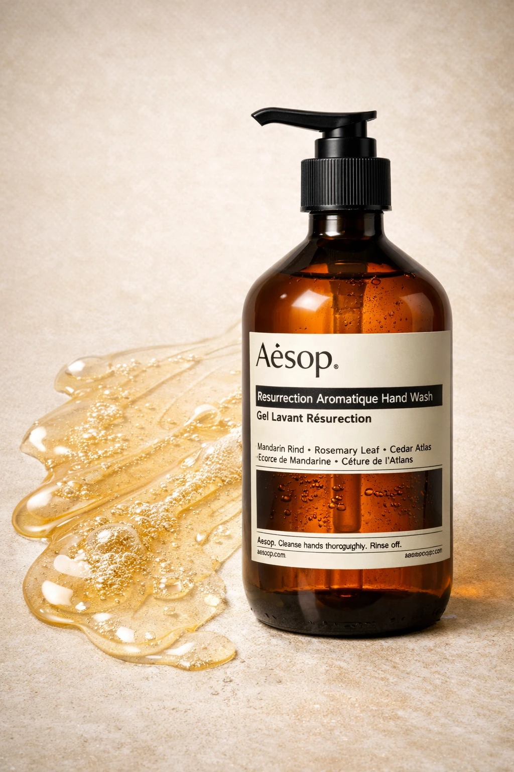 Aesop hand soap amber bottle with pump dispenser shown on neutral surface with liquid soap texture